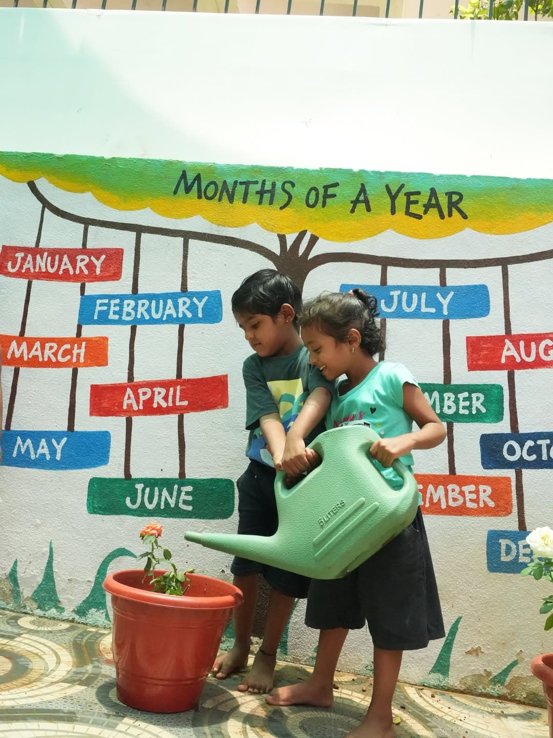 Children watering plants beside the colourful 'Months of a Year' learning wall.