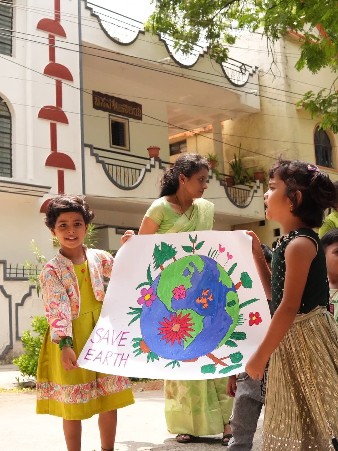 Children and their teacher holding a hand-painted 'Save Earth' poster.