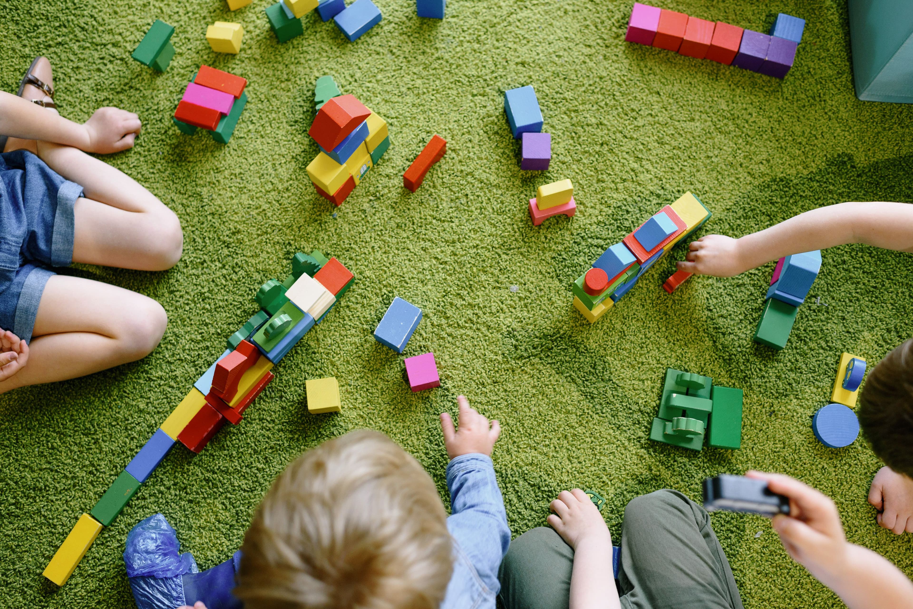 Children playing with colourful wooden building blocks on a green play mat.